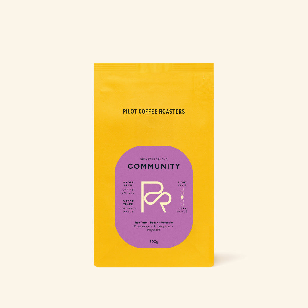 Bright yellow Community Blend bag standing upright with a purple label on a pale background