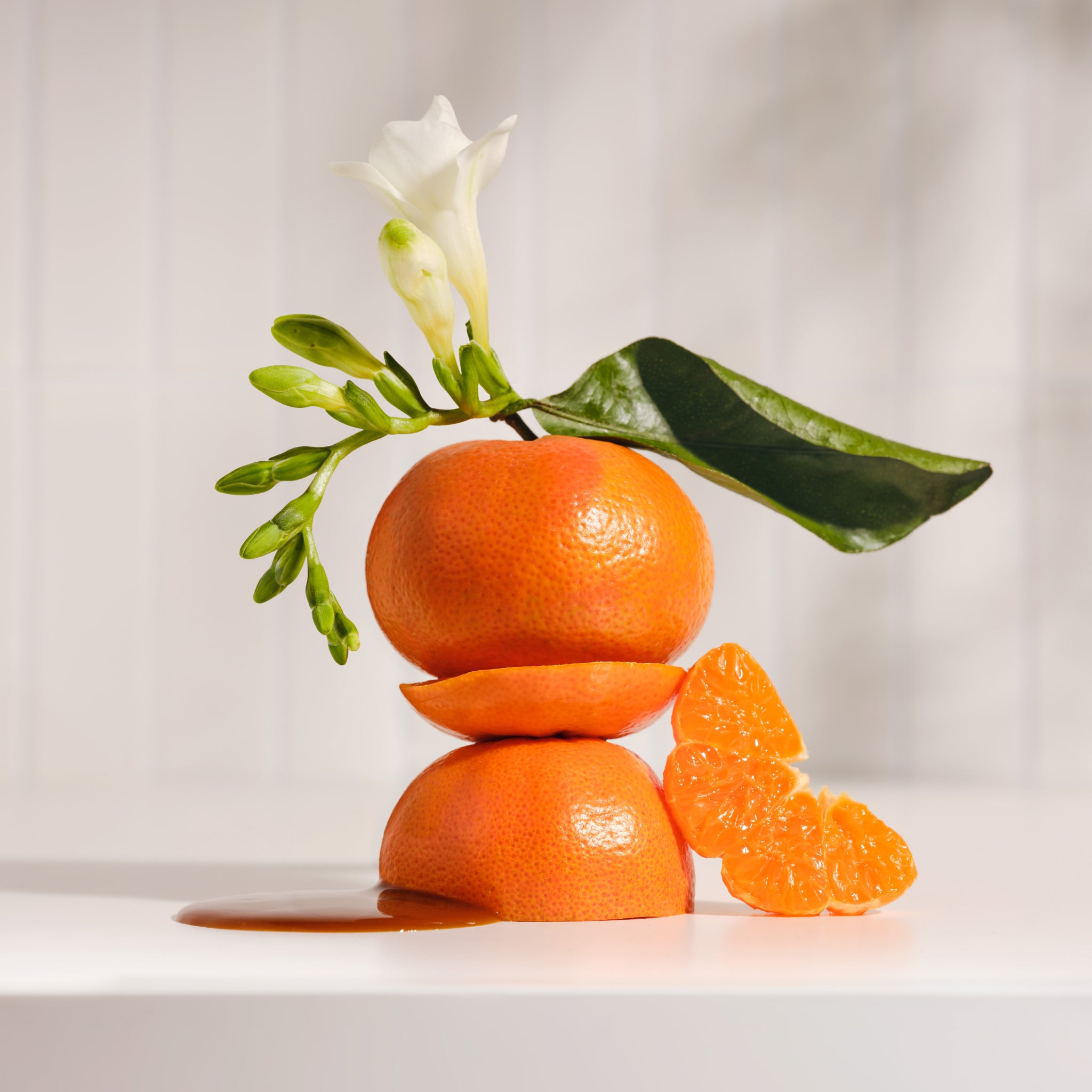 White blossom with green buds and a stack of oranges on a white countertop