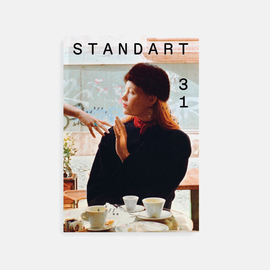 Standart Issue 31 magazine cover featuring a woman wearing a coat and hat, sitting at a table in a cafe with coffee cups on the table