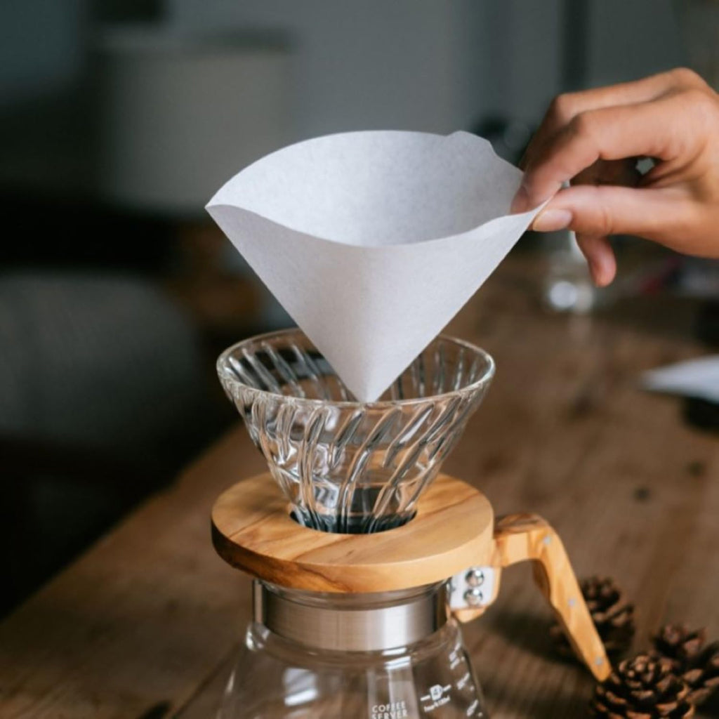 Person places a V60 paper filter into a glass pour-over dripper over a carafe.