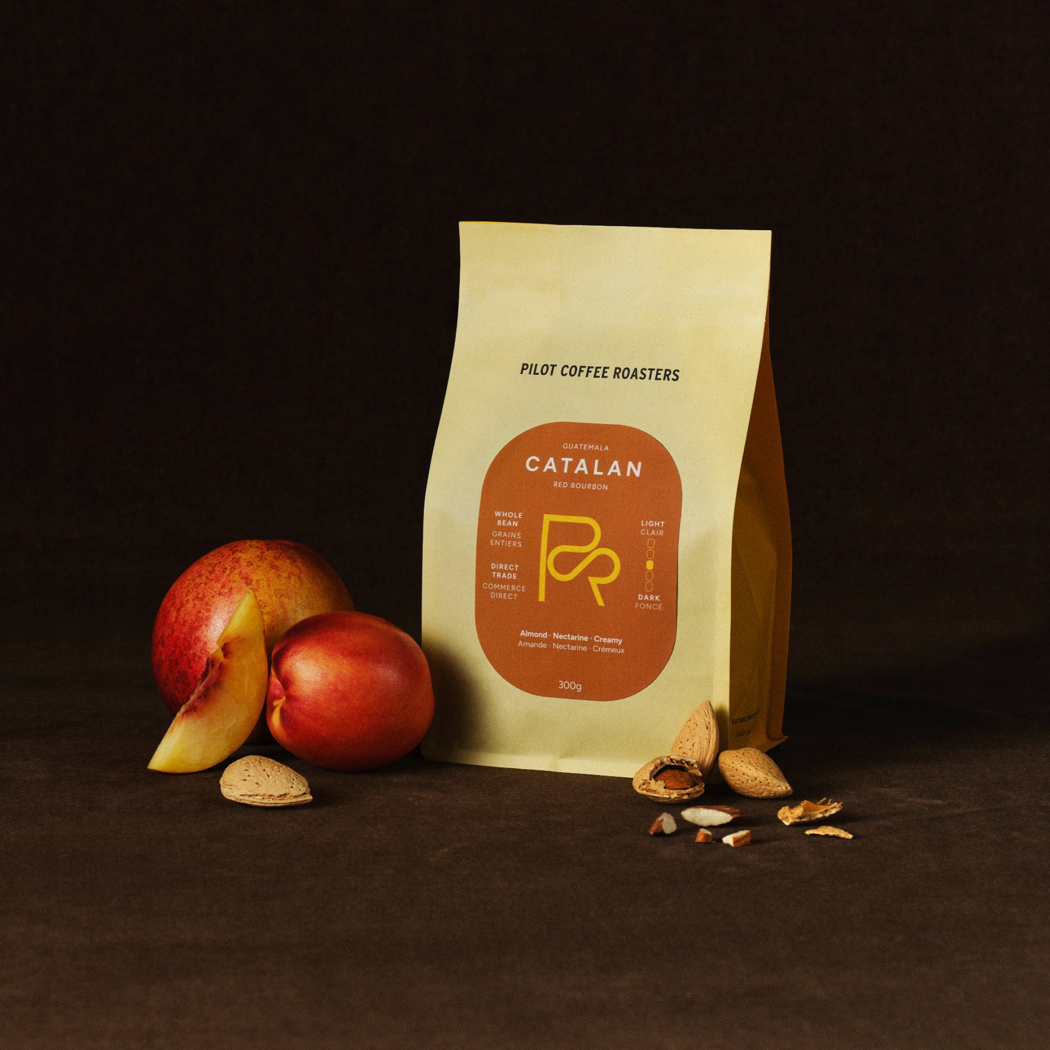 Catalan Red Bourbon Guatemala coffee bag against a dark background next to nectarines and whole almonds