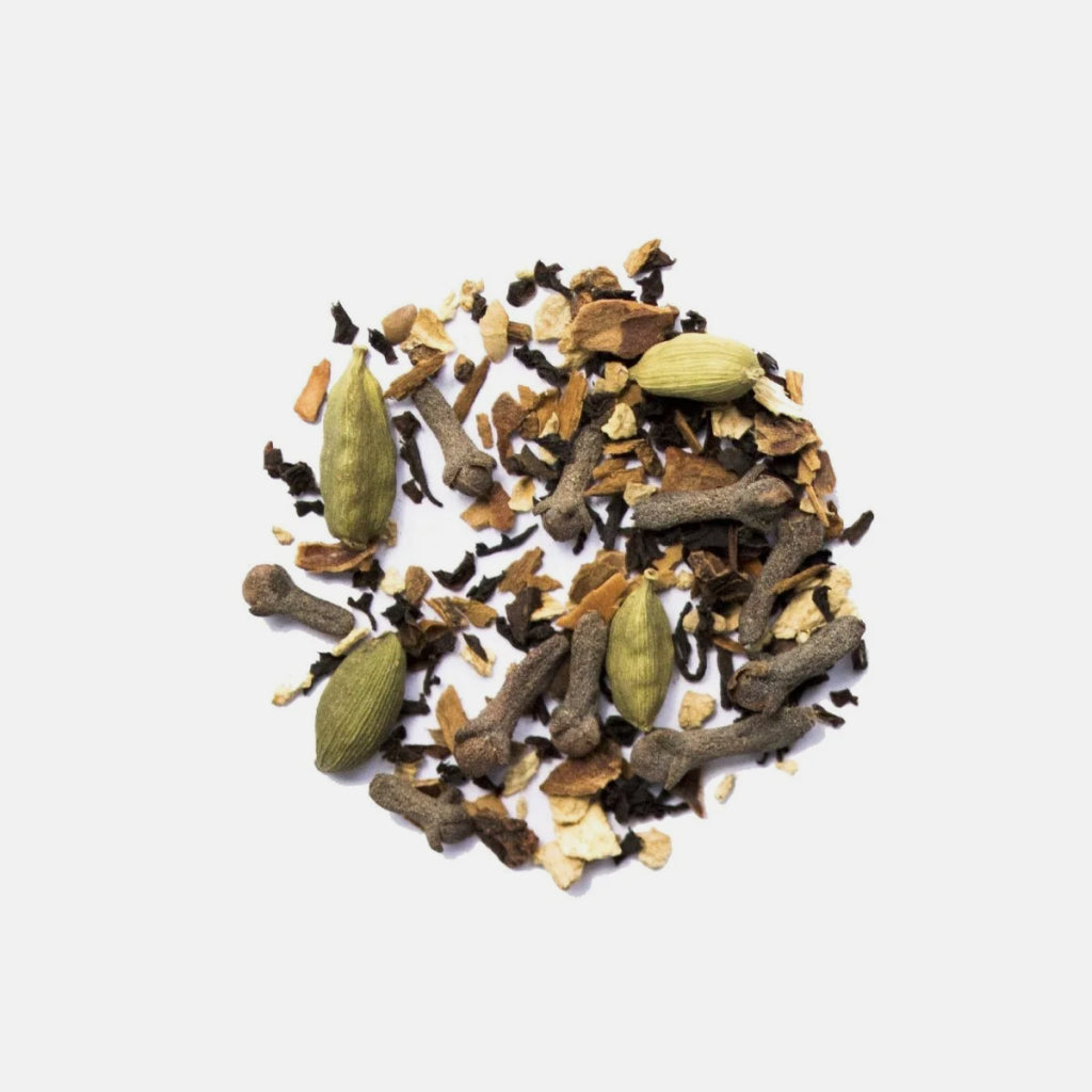 Loose masala chai spice blend with cardamom pods, cloves and dried citrus on a white background.