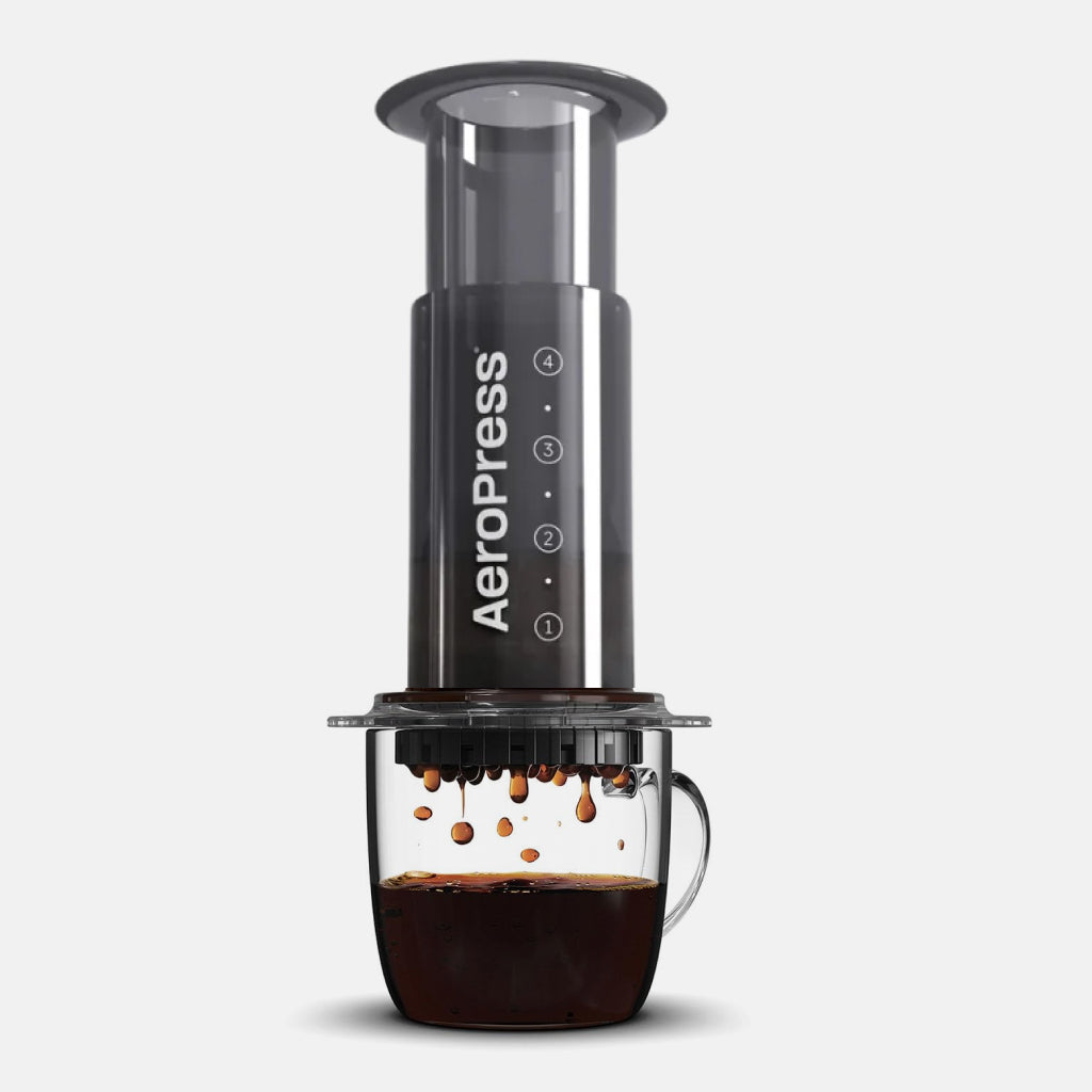 AeroPress coffee maker in translucent black, perched over a glass mug of coffee