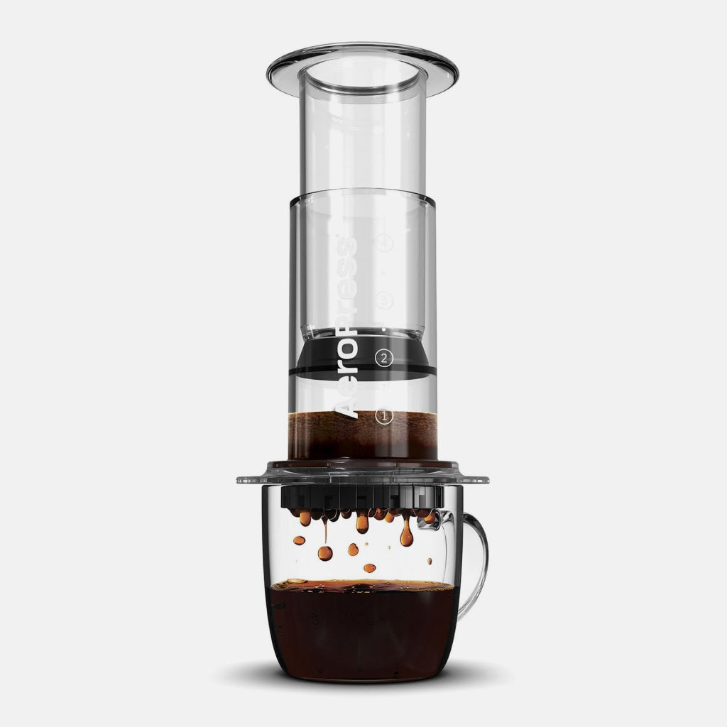 Clear AeroPress coffee maker brewing into a glass carafe beneath