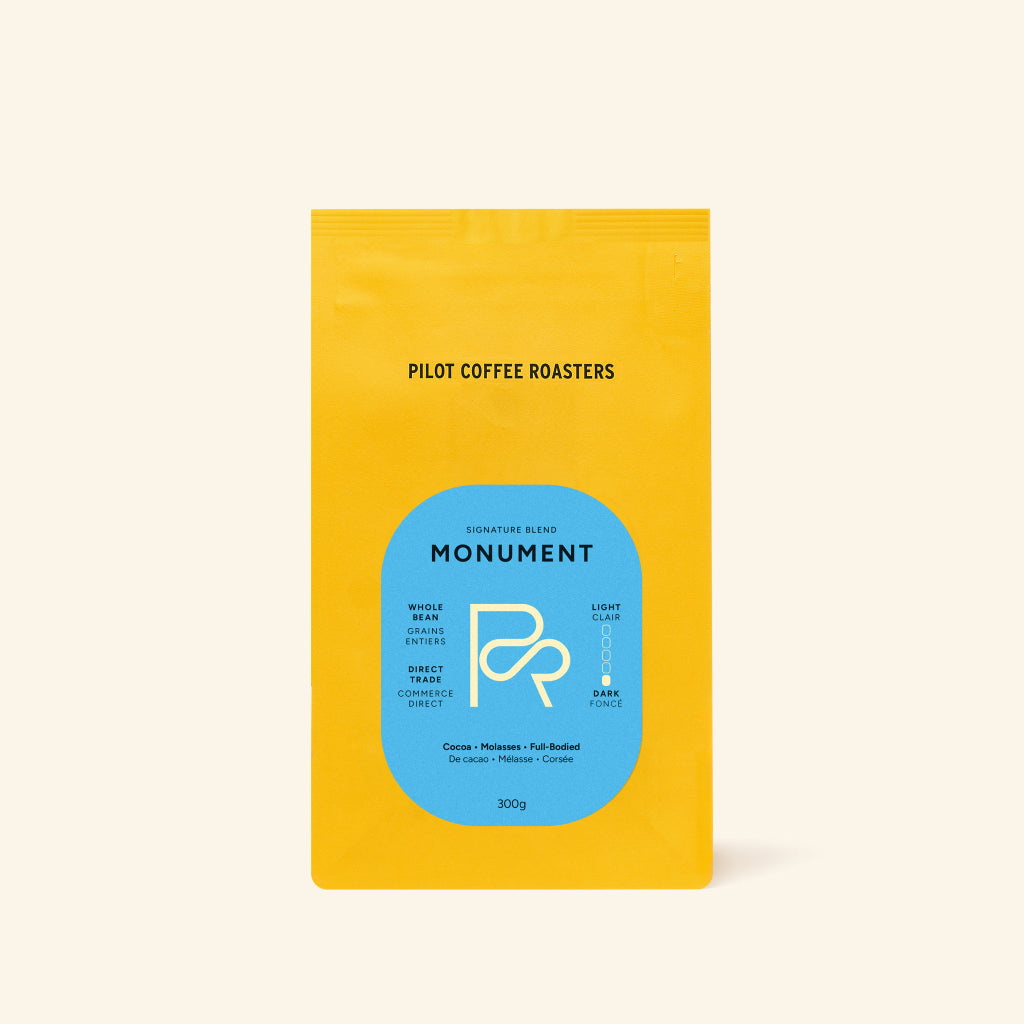 Monument coffee bag upright with yellow packaging and a blue label against a pale backdrop.