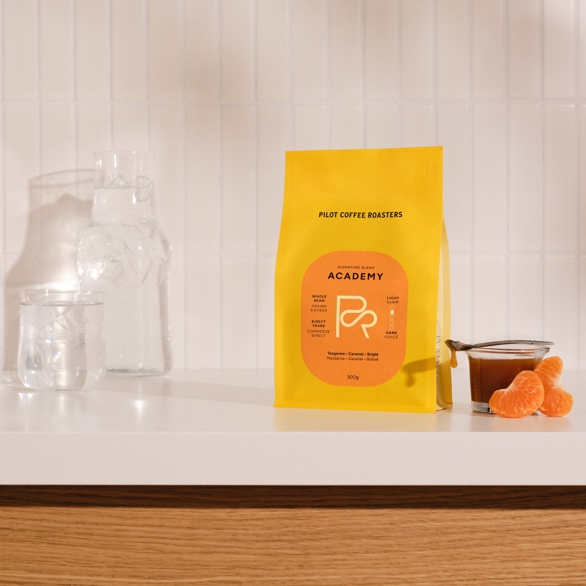 Academy coffee bag with bright yellow packaging on a white countertop beside glassware.