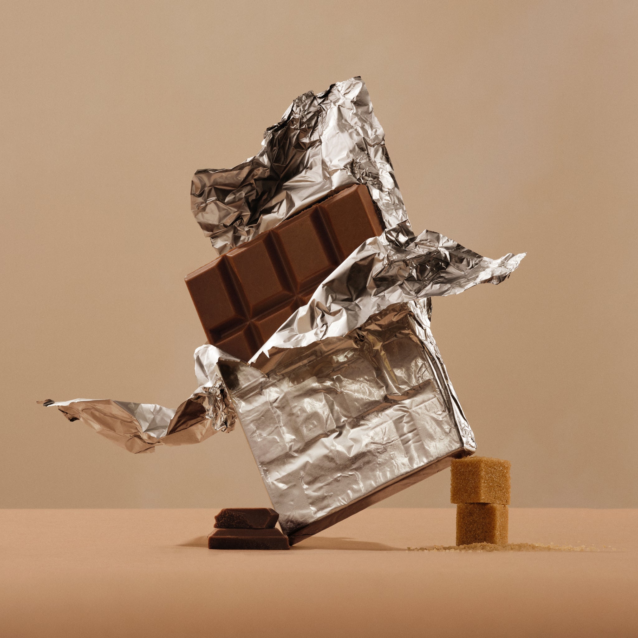 Crinkled foil wrapper around a chocolate bar with broken squares on a light background.