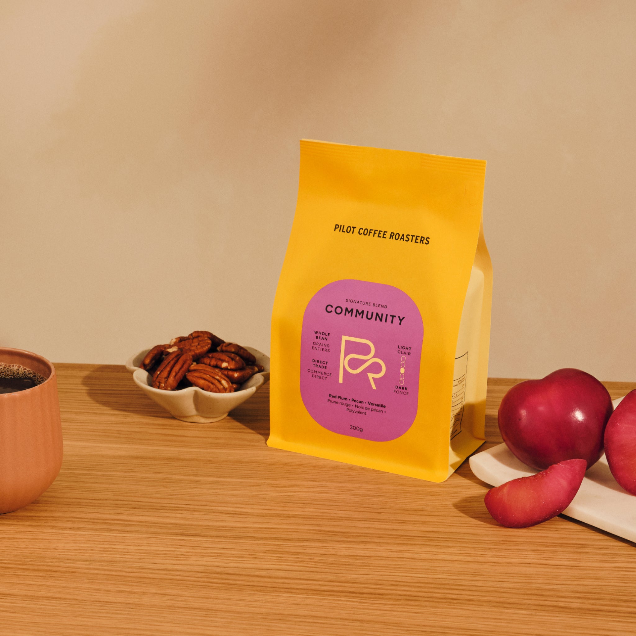 Bright yellow Pilot Coffee Roasters Community Blend bag on a wooden table with a bowl of pecans and plums