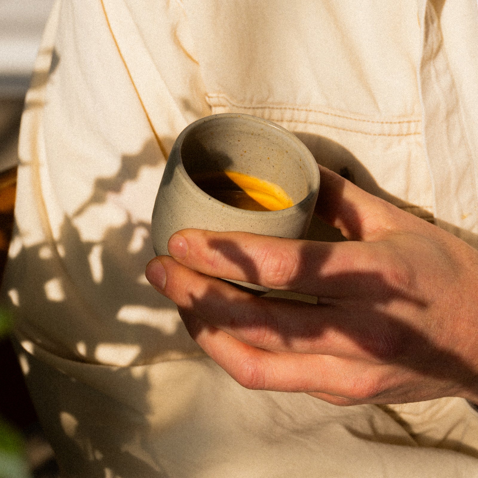 Hands cradle a small speckled ceramic espresso cup filled with espresso, in warm light.