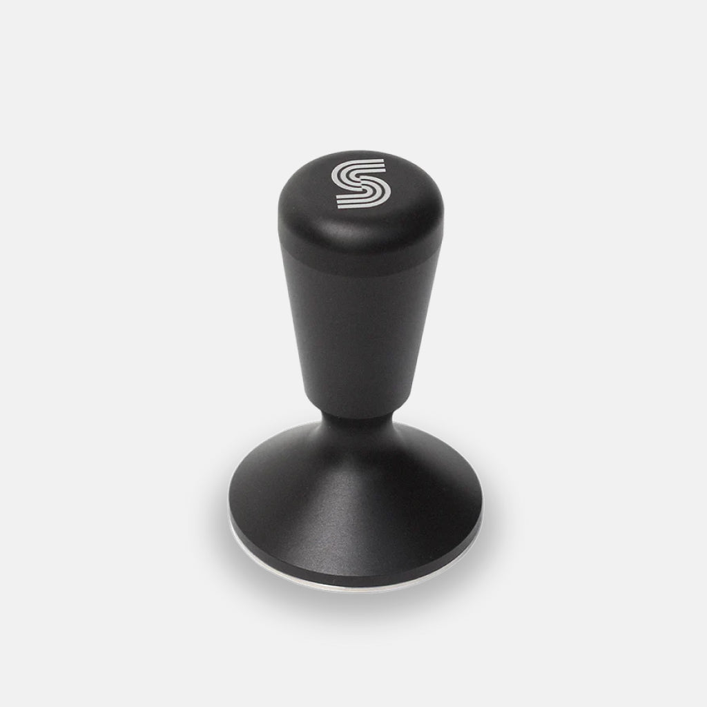 Matte black espresso tamper with slip resistant handle and flat metal base.