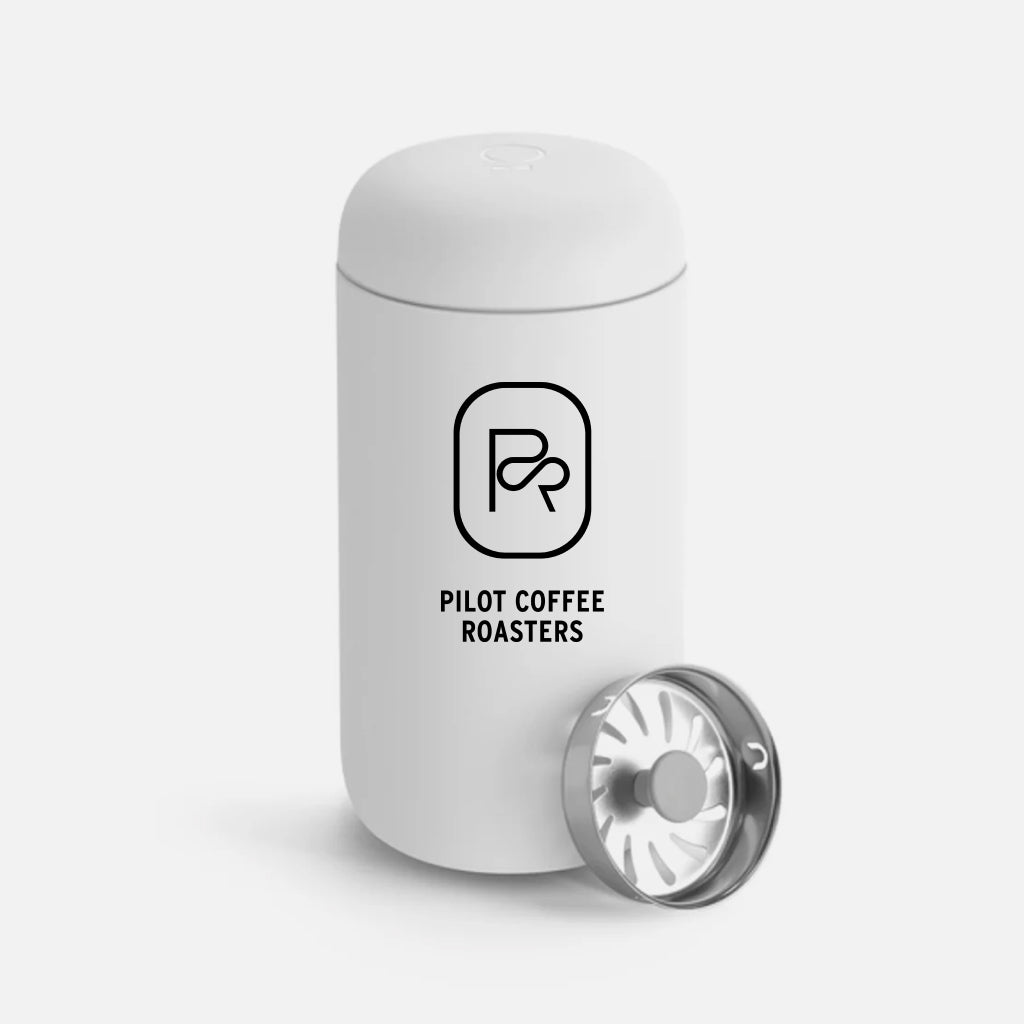 White Pilot Coffee Roasters travel mug with logo, and stainless steel splash guard resting beside it.
