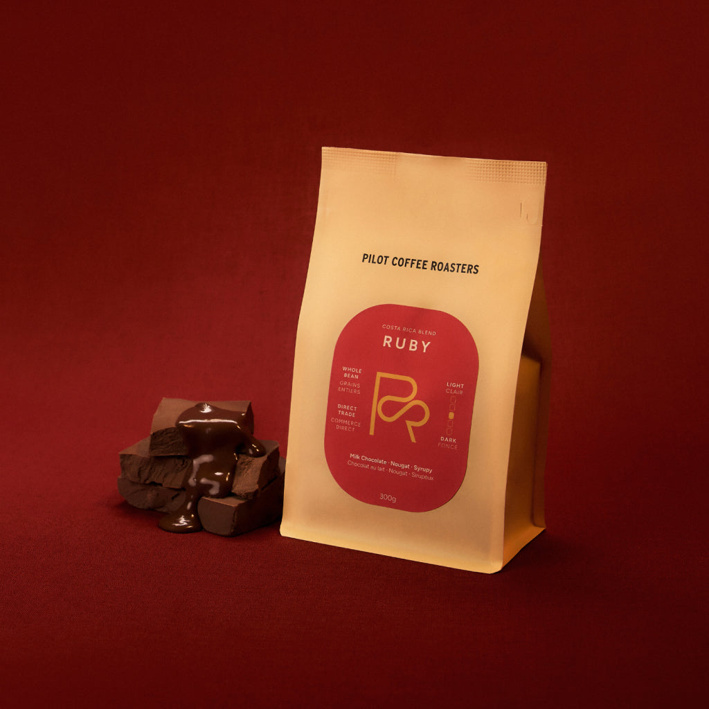 Ruby Costa Rica Blend bag with red label on a warm red backdrop beside chocolate pieces.