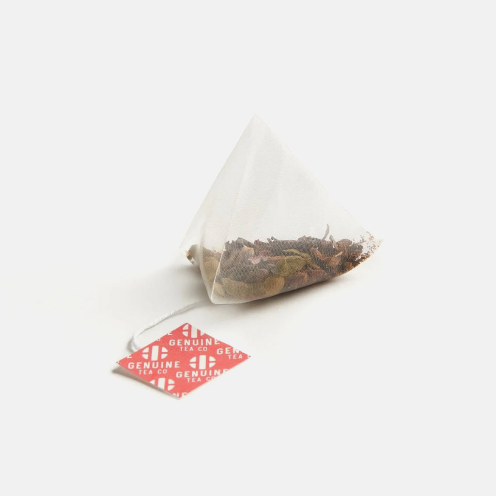 Pyramid tea bag filled with organic masala chai spices and tea, attached to a red Genuine Tea Co tag.
